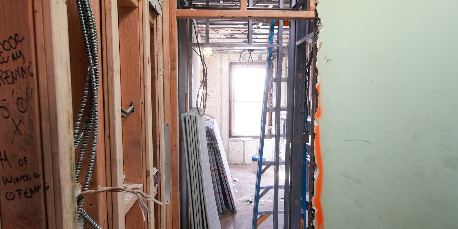Active whole home remodel jobsite - gut to studs interior with framing, electrical conduit, drywall stack, and handwritten scope notes on the wall